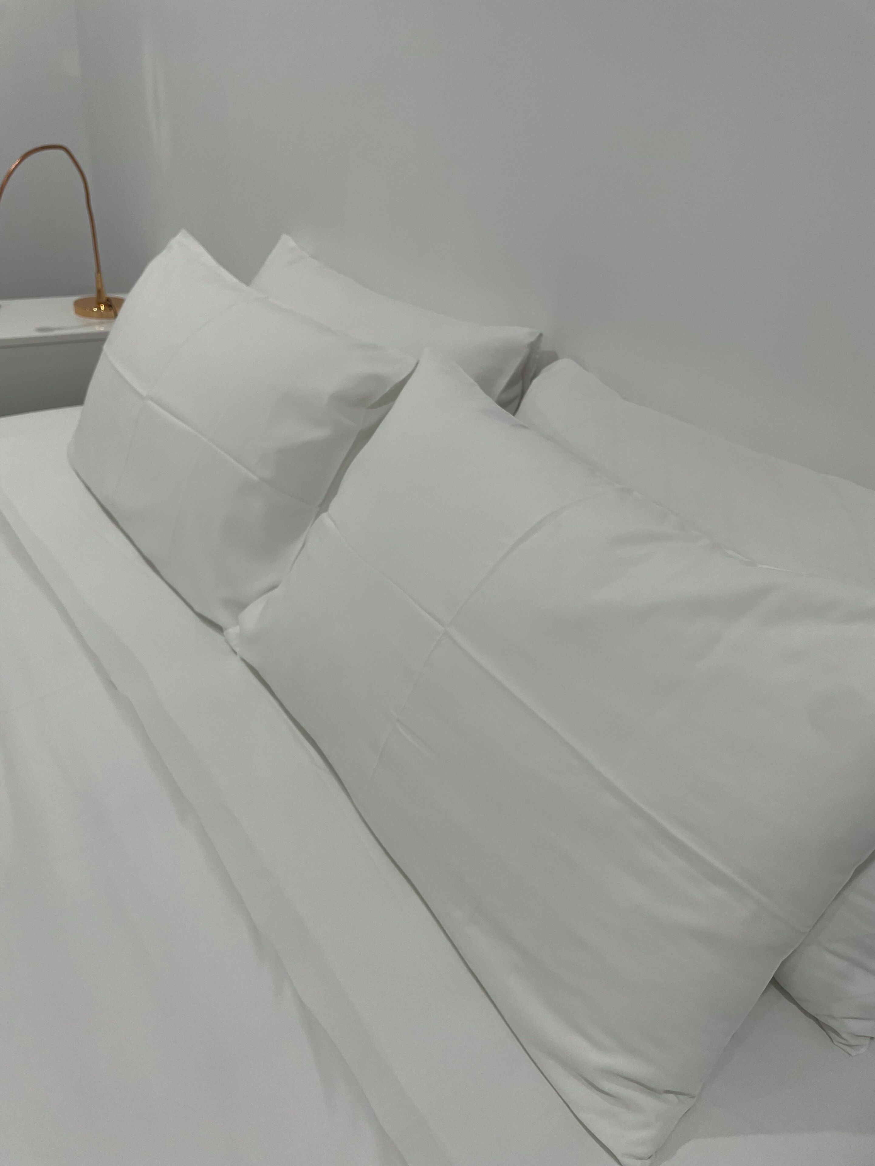 A bed with white bedding and a bedside table with a lamp.