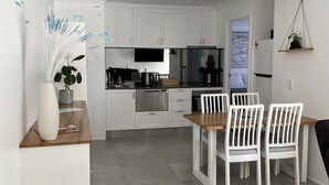 A modern kitchen with white cabinets, a dining area with white chairs, and a small plant on the wall.