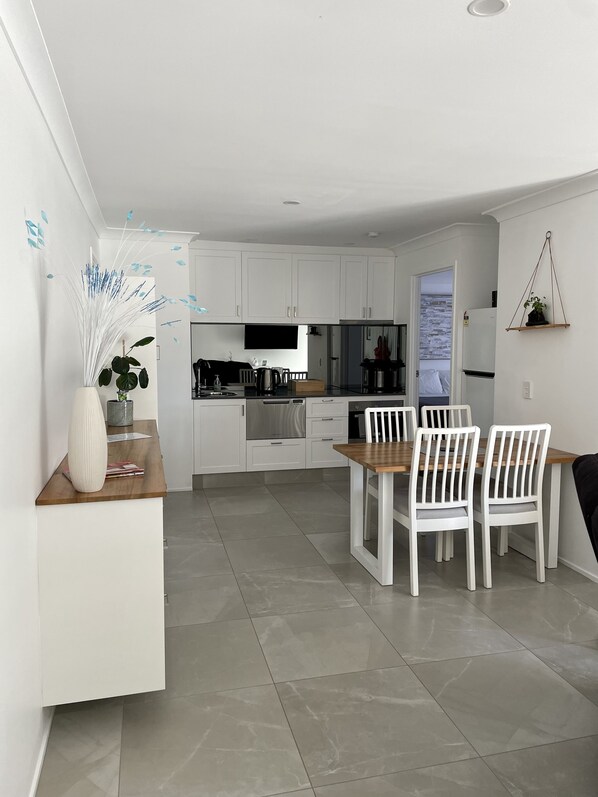 Une cuisine moderne avec des meubles blancs, un coin repas avec des chaises blanches et une petite plante accrochée au mur.