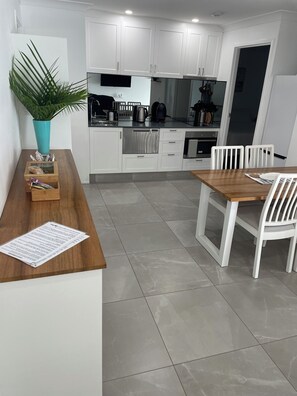 Une cuisine moderne avec des meubles blancs, un plan de travail en bois et un coin repas avec des chaises blanches.