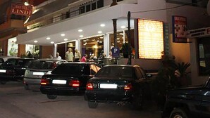 Et flereetagers hotel med en markant rød og hvid facade, flere balkoner og en parkeringsplads med flere biler.
