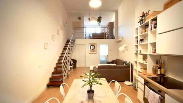 A modern apartment with a wooden dining table, white chairs, a kitchen with a stove, and a staircase leading to an upper level. - Loft in Florence/Boboli with reserved garage parking space (Firenze)