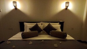 A neatly made bed with pillows and a dark bedspread, two wall-mounted light fixtures, and a small flower on the bed. - The most comfort rest starts here (Habaraduwa)