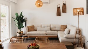 Un salon chaleureux avec un canapé beige, une table à manger en bois sur laquelle se trouve un saladier rempli de fruits, une grande plante et un lampadaire.