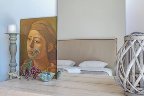 Un dormitorio con una cama, un adorno en la pared, una mesita con una vela y una cesta de mimbre.