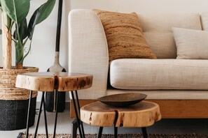 Un salon moderne avec un canapé blanc, deux petites tables en bois, un panier en osier et une plante en pot.