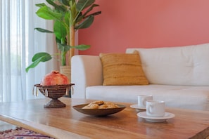 Una sala de estar acogedora con una mesa de centro de madera, un cuenco de bocadillos, una planta decorativa y un sofá blanco con un cojín.