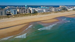 An aerial view of a coastal hotel area with multiple buildings, a sandy beach, and a clear view of the ocean. - Enjoy beautiful ocean views at this 3 bedroom, 2 bath oceanfront condo located downtown! (Ocean City)