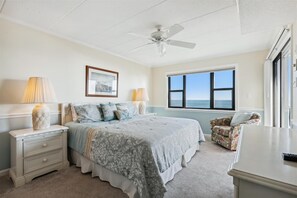 A bedroom with a bed, bedside lamps, a ceiling fan, a framed picture, a window with a view, and a chair. - Enjoy beautiful ocean views at this 3 bedroom, 2 bath oceanfront condo located downtown! (Ocean City)