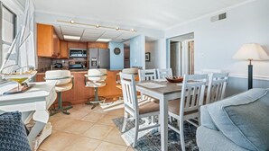 A modern kitchen with wooden cabinets, a microwave, and a refrigerator. There is a dining area with a table and chairs, and a lamp on the right. - Enjoy beautiful ocean views at this 3 bedroom, 2 bath oceanfront condo located downtown! (Ocean City)