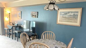 A dining area with a round table and six chairs, a television, and a wall-mounted lamp.