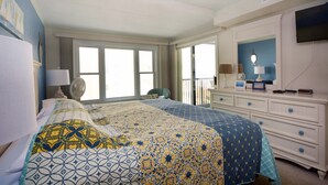 A hotel room with a large bed, a dresser, a television, and a window with curtains.