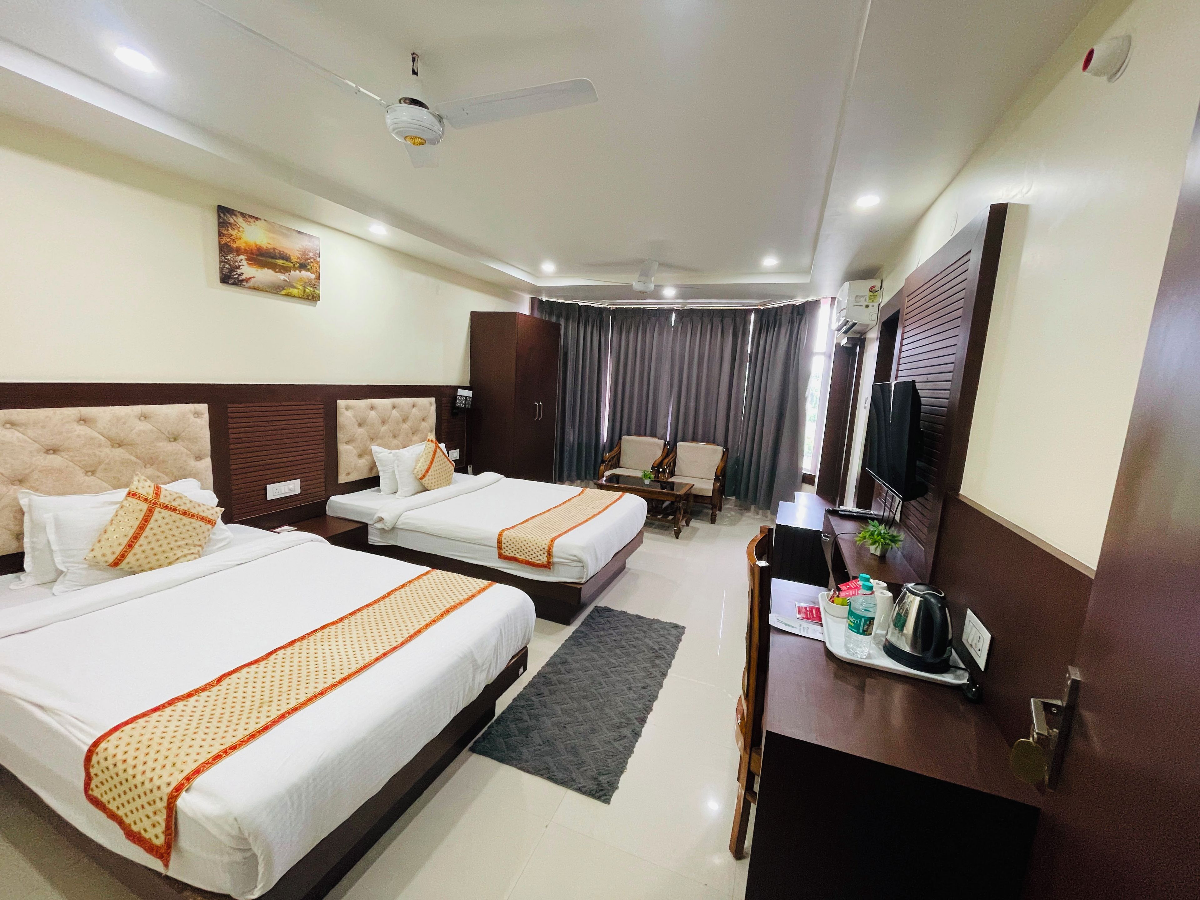 A hotel room with two beds, a desk, a chair, a television, and a ceiling fan.