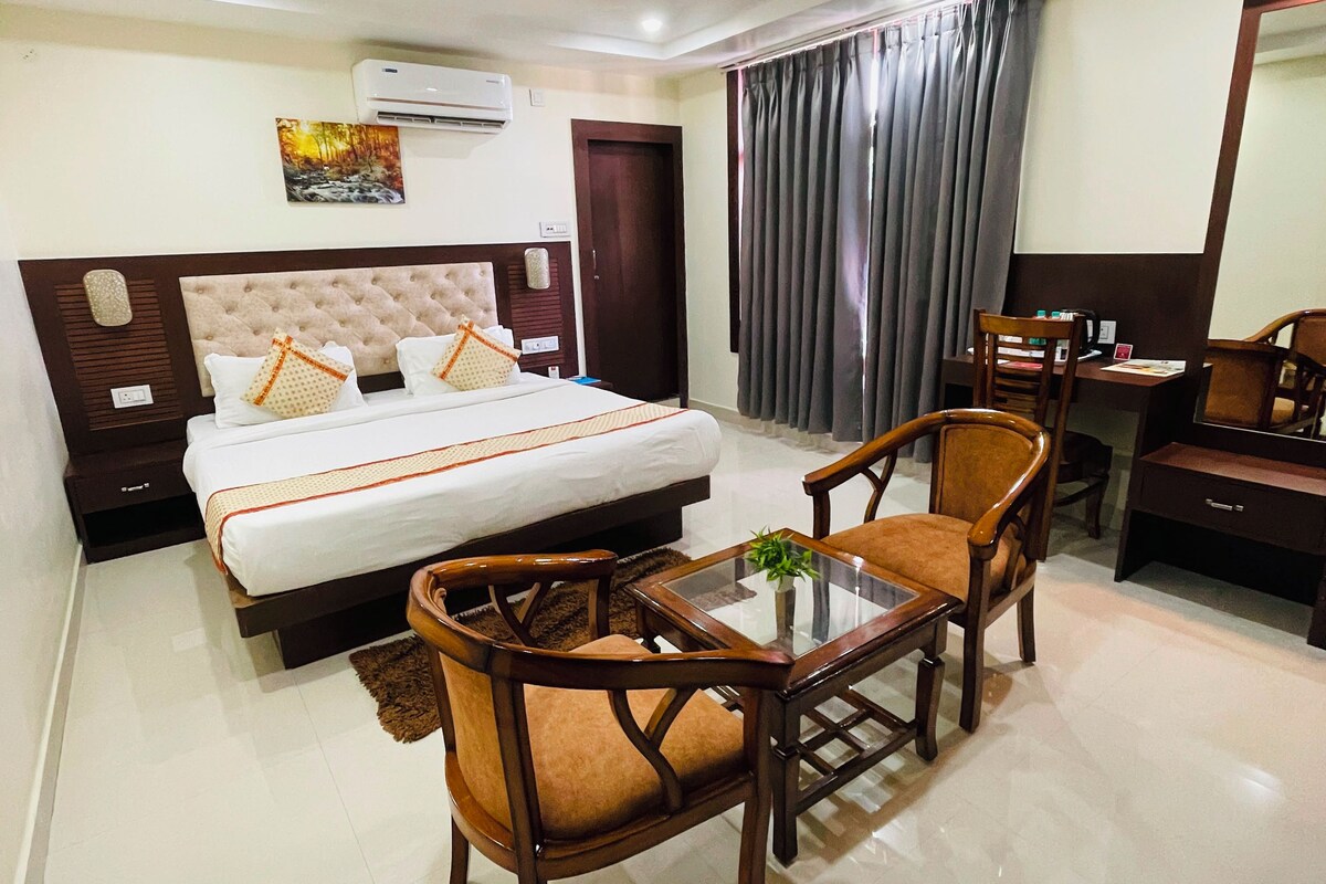 Habitación de hotel con cama, dos sillones, escritorio y espejo.