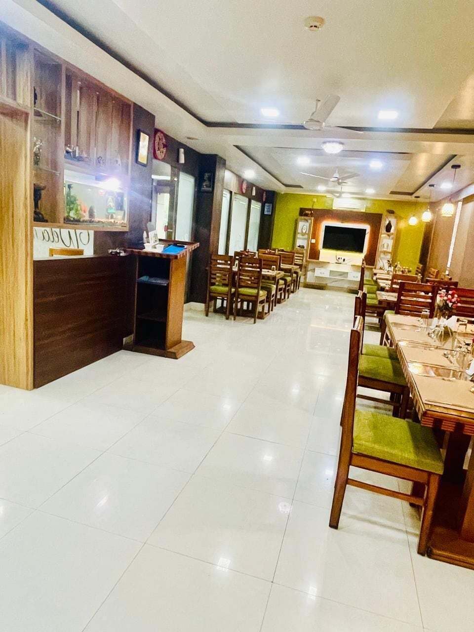 A restaurant with a counter, multiple tables, chairs, and a television screen.