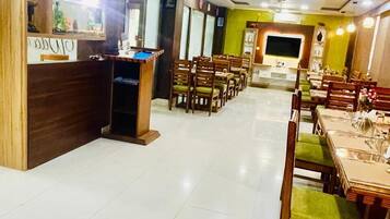 A restaurant with a counter, multiple tables, chairs, and a television screen.