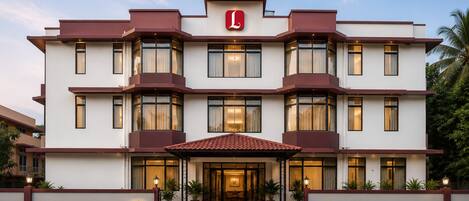 A multi-story hotel with a prominent red and white color scheme, featuring a large entrance with a tiled roof and potted plants.