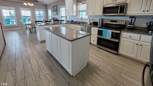 Una cocina amplia con una isla grande, armarios blancos y electrodomésticos modernos.