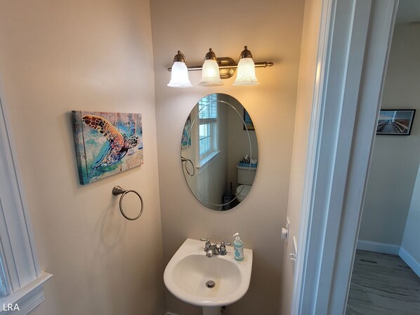 Une salle de bain avec un miroir rond, un lavabo et un porte-serviettes. Il y a un tableau au mur et une fenêtre au-dessus du miroir.