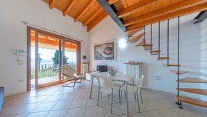 Un'ampia stanza con soffitto in legno, una zona pranzo con tavolo e sedie, una scala e un'ampia finestra con vista.