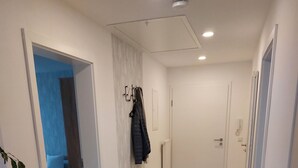 Käytävä, jossa on puulattia, musta matto ja takkien ripustamiseen tarkoitettu naulakko.