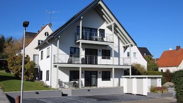 Ein modernes Wohngebäude mit zwei Etagen, einem Balkon, einer überdachten Sitzgelegenheit im Freien und einem befahrbaren Eingangstor.