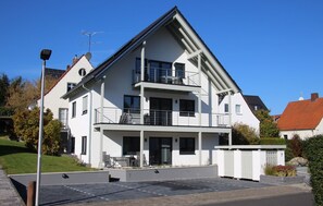 Un immeuble résidentiel moderne à deux étages, doté d’un balcon, d’un espace extérieur aménagé et couvert, et d’une entrée sécurisée par un portail.