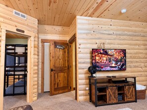 A log cabin interior with a bunk bed, a television mounted on the wall, and a cozy cabin sign.