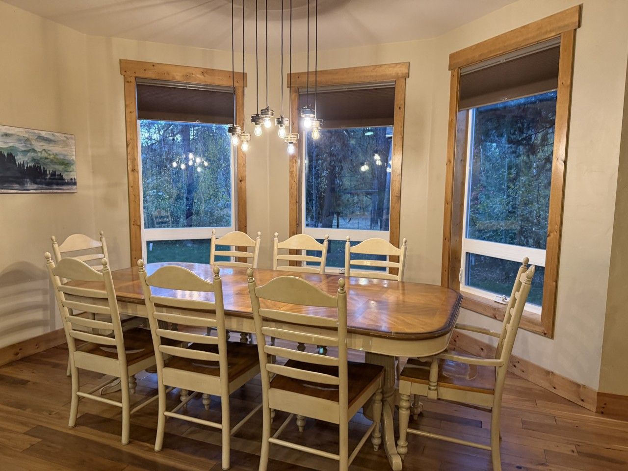 Een eethoek met een houten tafel, stoelen, grote ramen en hanglampen.
