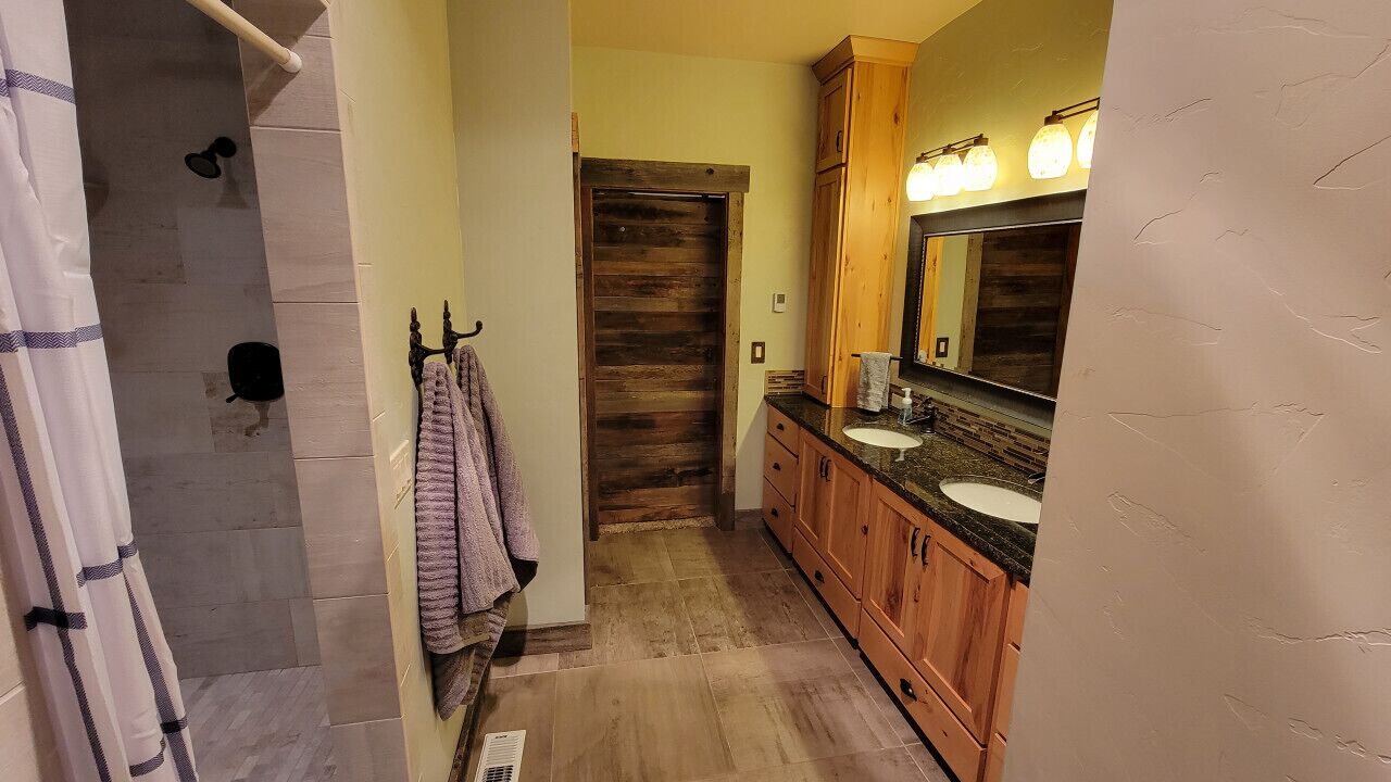 A bathroom with a wooden door, a sink with a mirror, and a shower area.