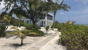 Une propriété située en bord de mer, avec un chemin en béton menant à un bâtiment doté d’un balcon.