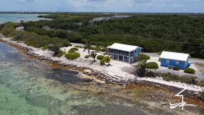 Une propriété située sur la côte, avec deux bâtiments bleus, une plage de sable et une vue dégagée sur l’océan.