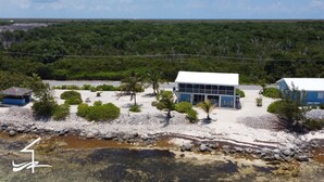 Un bâtiment situé sur la côte, avec un toit blanc, entouré d’une végétation clairsemée et bordé d’un rivage rocheux.