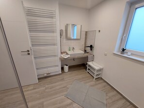 Ein modernes Badezimmer mit Waschbecken, Spiegel und Handtuchhalter. Ein Fenster bietet Blick auf den Himmel, und ein kleiner Topf steht auf der Fensterbank.