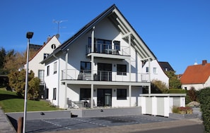 A modern two-story residential building with a balcony, a covered outdoor seating area, and a gated entrance. - Barrier-free vacation apartment Königsquelle (Bad Wildungen)