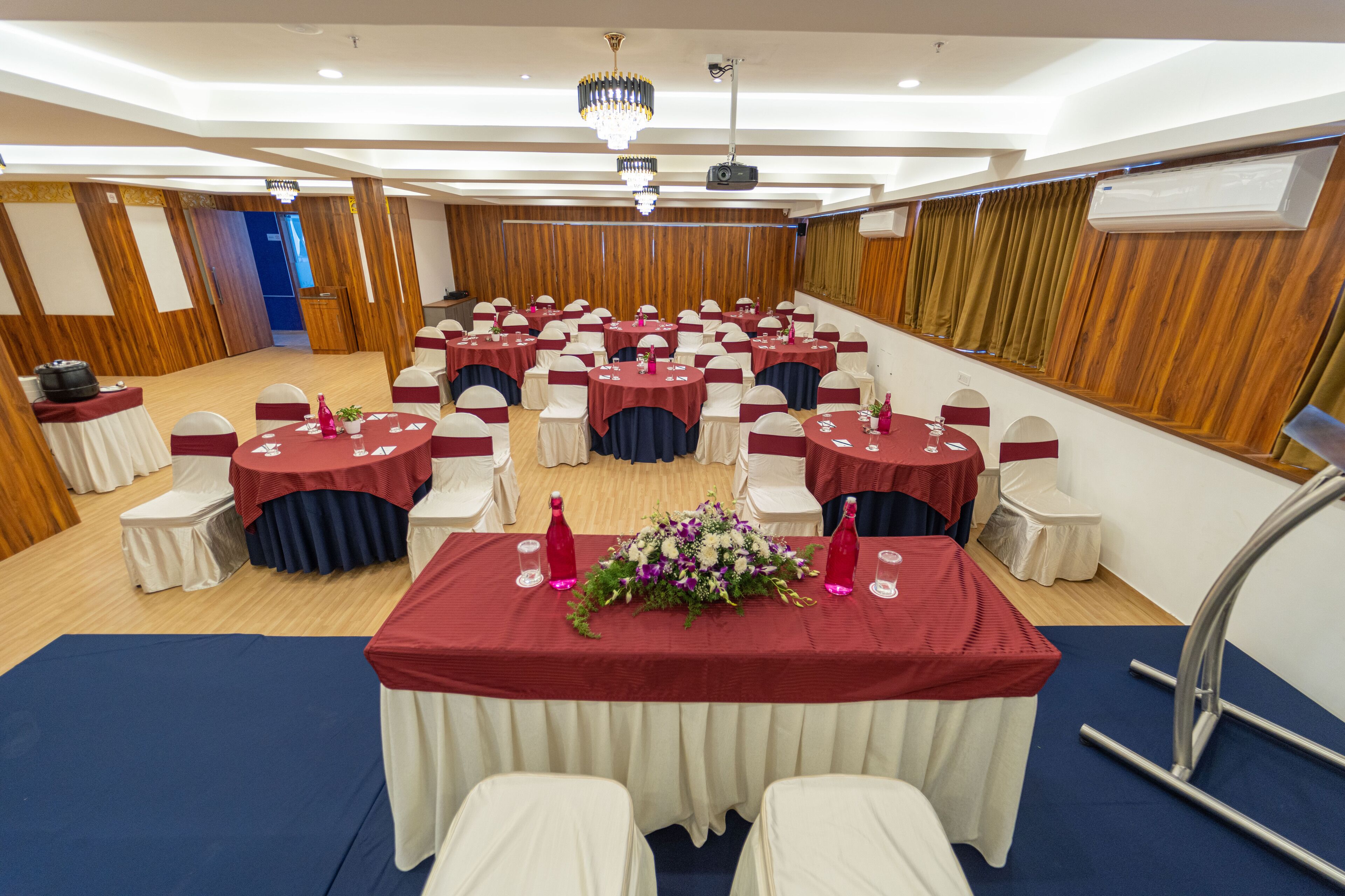 A banquet hall with round tables, white chairs, and red tablecloths.