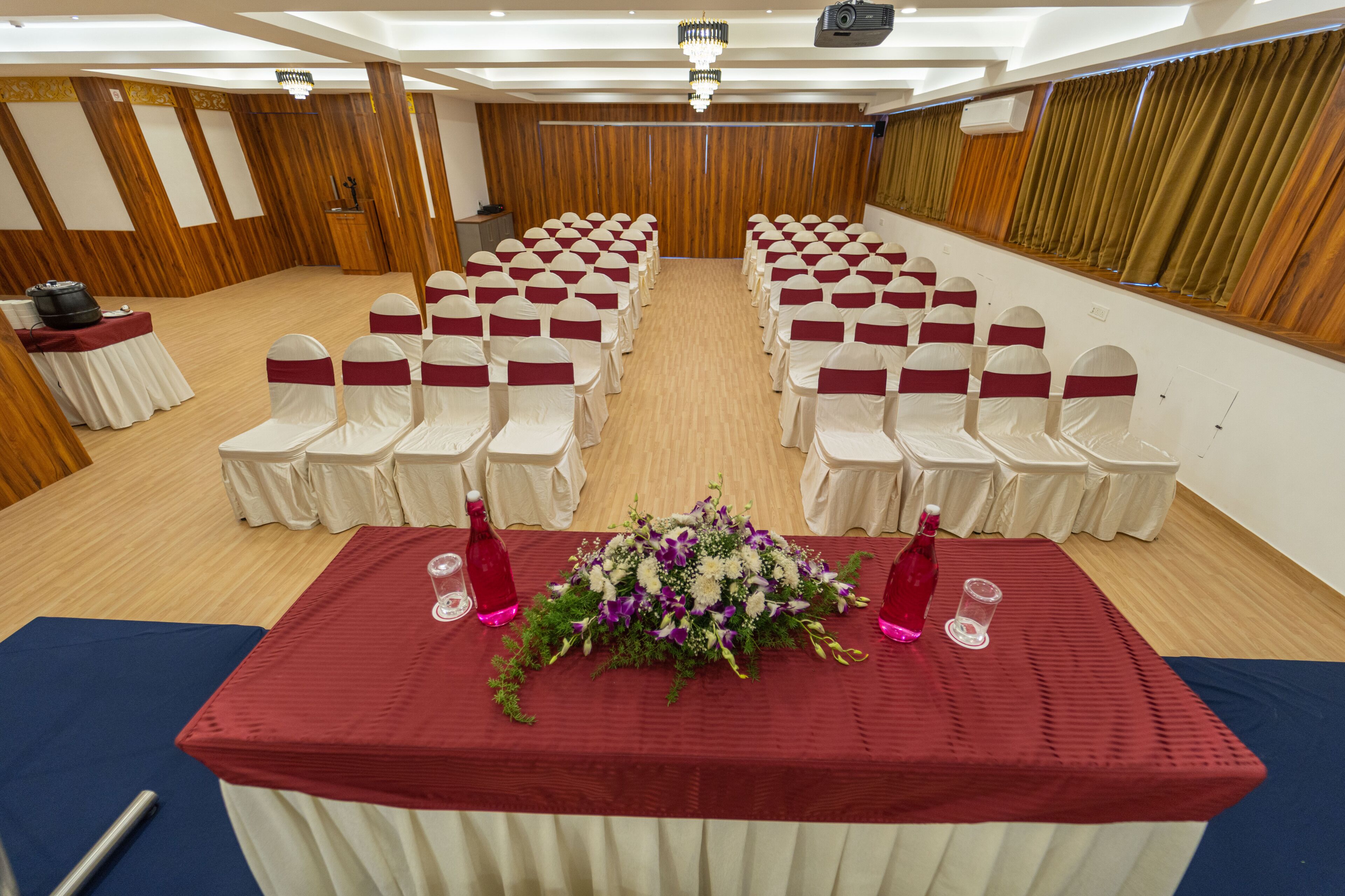 A conference room with rows of chairs, a table with a floral centerpiece, and a podium.