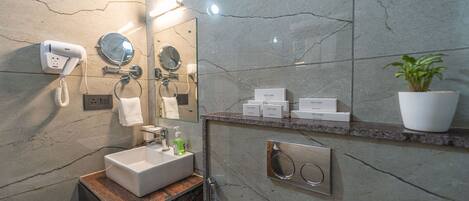 A modern bathroom with a marble sink, a handheld showerhead, a hairdryer, and a potted plant.