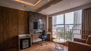 Et moderne hotelværelse med trævæg, en marmorvæg som detalje, et fladskærms-tv, et lille køleskab, et skrivebord, en stol, et rundt bord og en sofa.