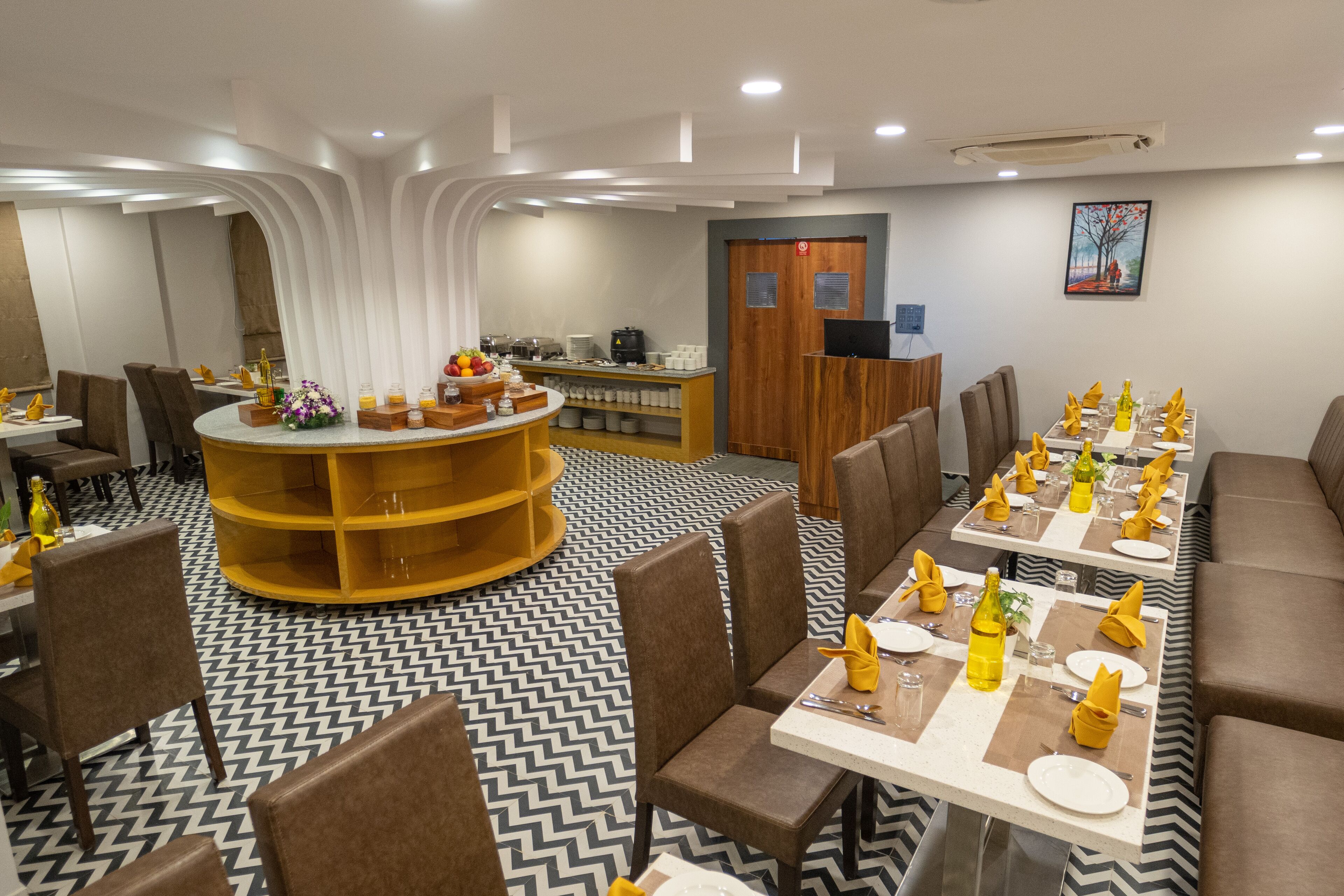 Un espace de restauration moderne avec une table ronde centrale, de nombreux types de sièges et un sol à motifs.