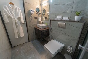 A modern bathroom with a marble vanity, a white sink, a handheld showerhead, a toilet, and a robe hanging on a door. - Clarks Inn, Airport Bangalore (Bengaluru)