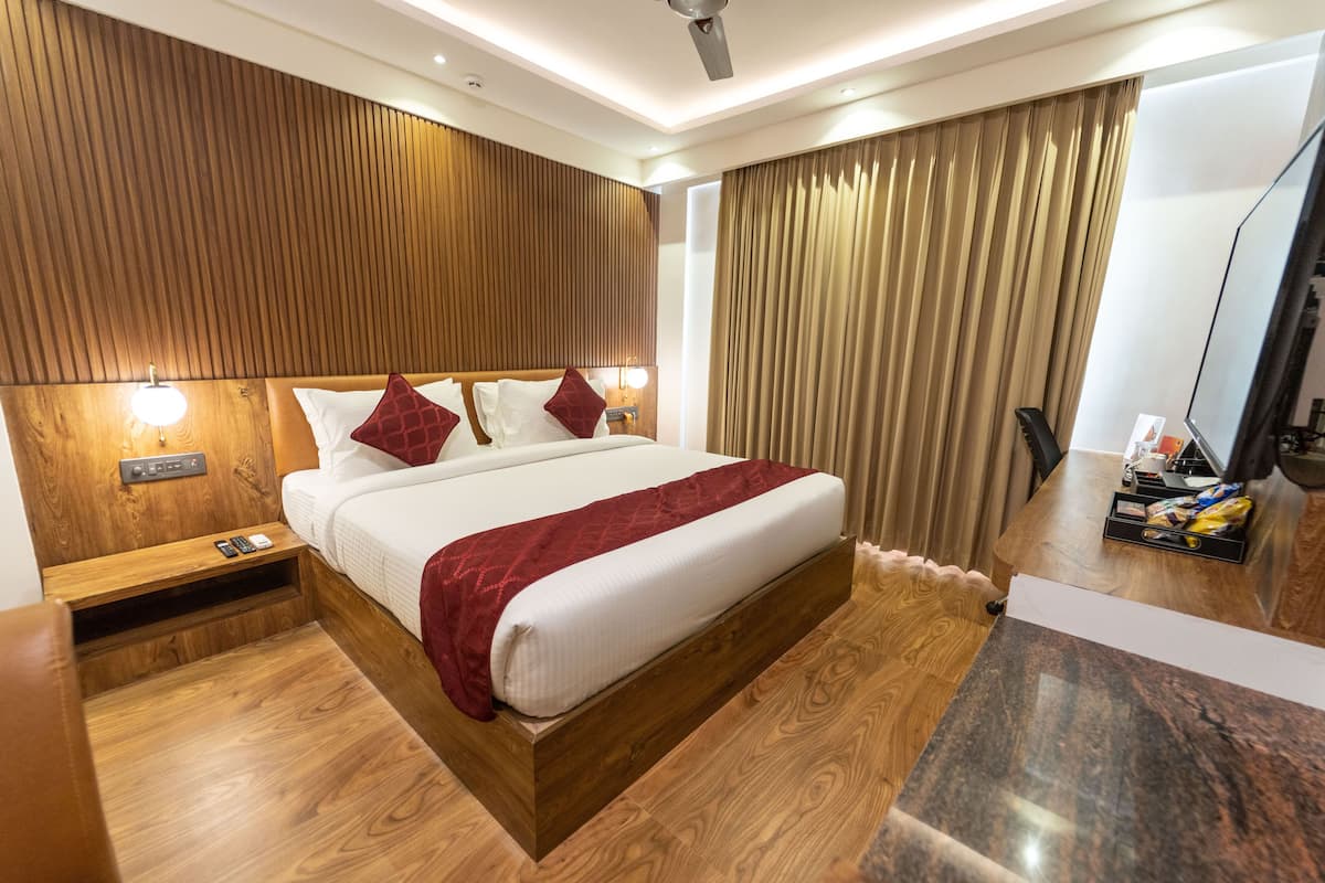 A modern hotel room with a wooden headboard, a large bed with white linens and red accents, a bedside table with a lamp, and a large mirror on the wall.