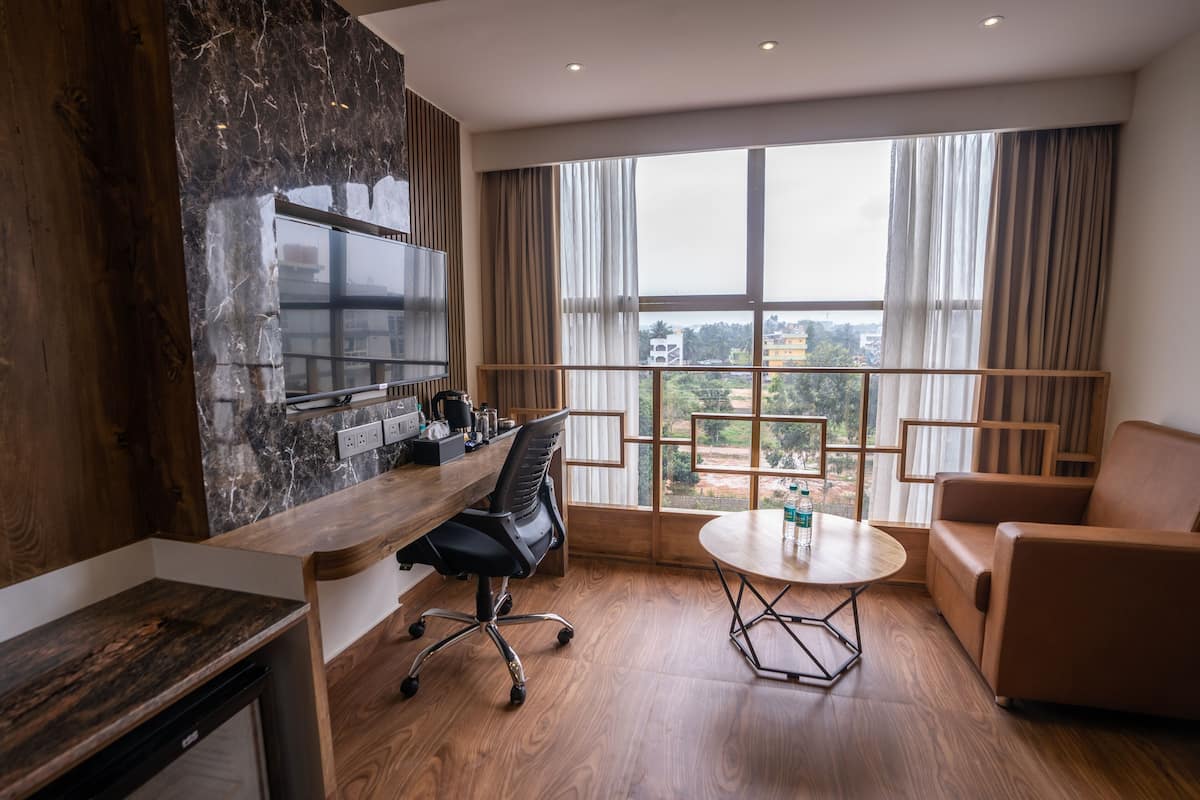 A modern room with a wooden desk, a black office chair, a round table, and a brown sofa.
