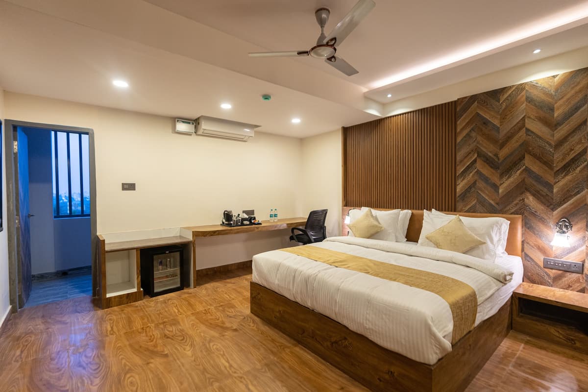 A modern hotel room with a wooden floor, a large bed with white bedding, a desk with a chair, and a ceiling fan.