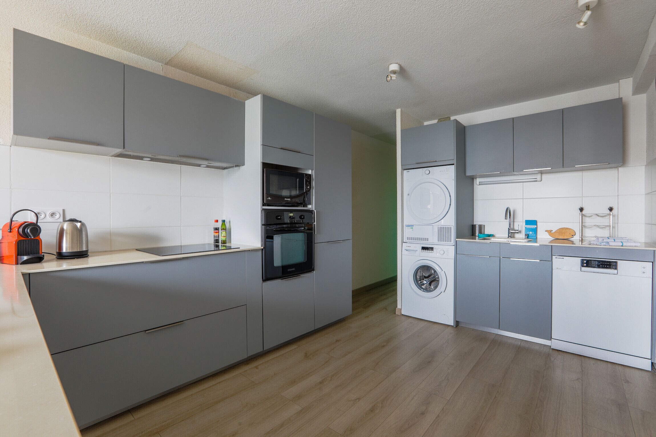 Une cuisine moderne avec des meubles gris, un four encastré, un micro-ondes, un lave-linge et un lave-vaisselle.