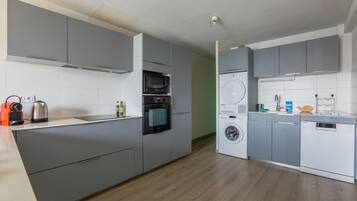 Une cuisine moderne avec des meubles gris, un four encastré, un micro-ondes, un lave-linge et un lave-vaisselle.