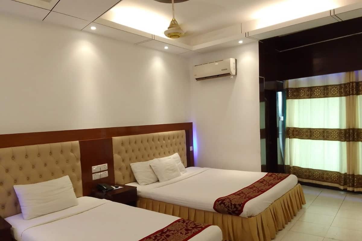 Une chambre d’hôtel avec deux lits, une table de chevet, un appareil de climatisation et une fenêtre avec des rideaux.