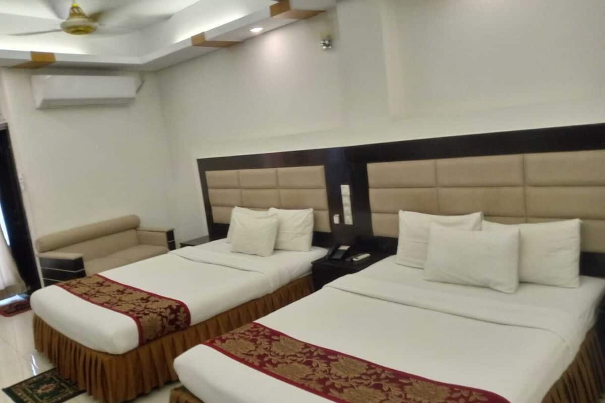 Une chambre d’hôtel avec deux lits, un canapé, un ventilateur de plafond et une petite table.