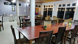 Un vaste espace dédié à la salle à manger, avec une grande table en bois entourée de chaises, une plante en pot et une vue sur le ciel nocturne grâce à de grandes fenêtres.