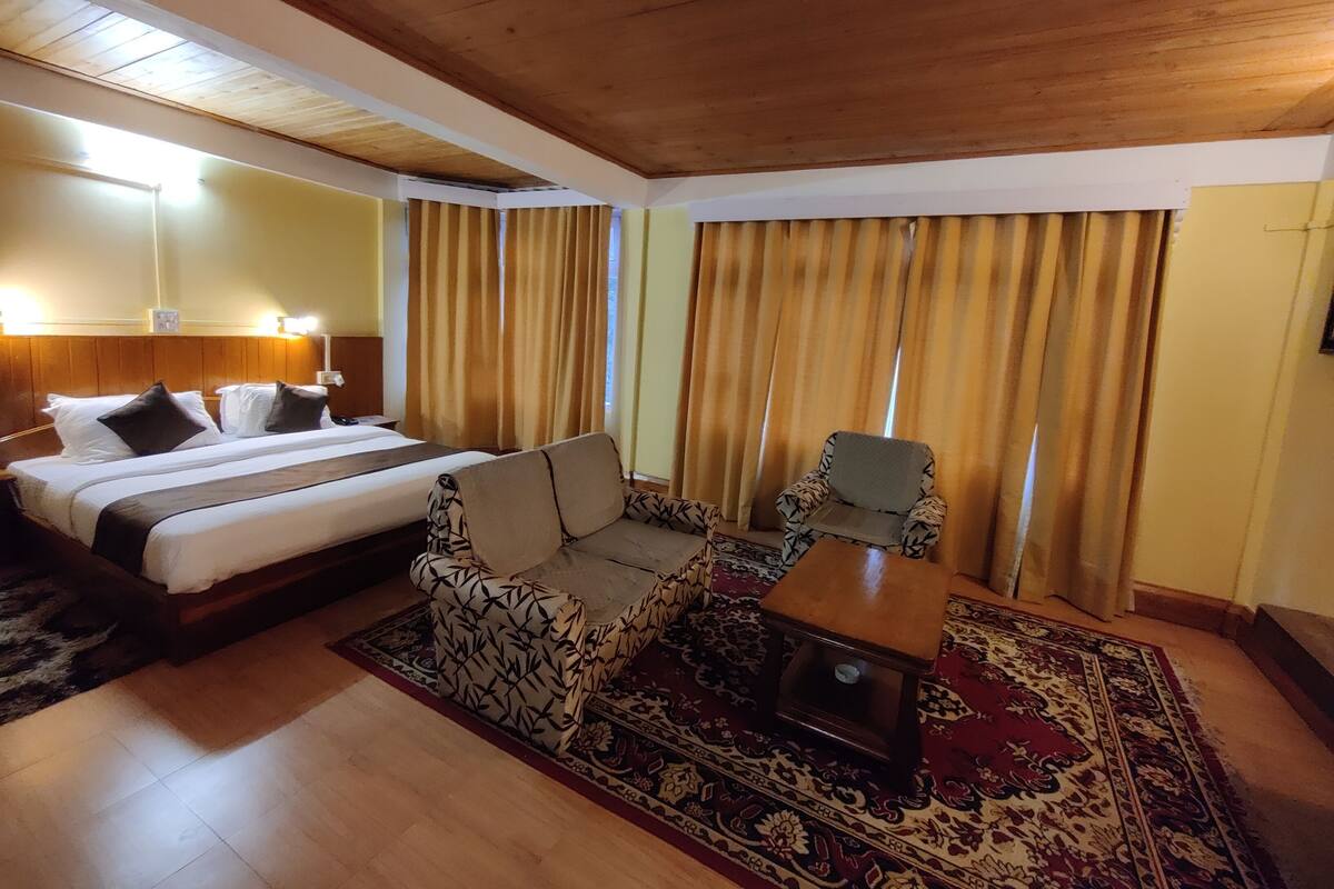 Una habitación de hotel con cama, sofá, una mesita y alfombra estampada.